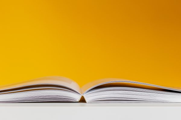 End-on photo of a book lying open on a white table, in front of a yellow wall
