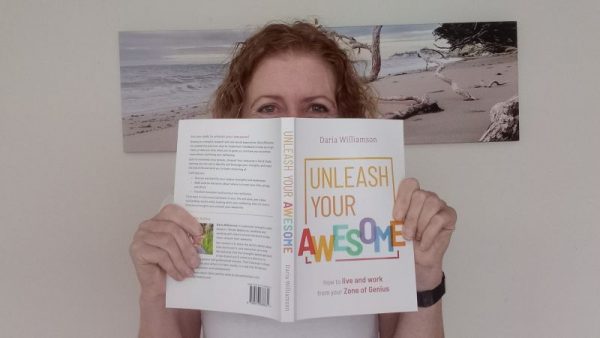Photo of a woman holding a copy of Unleash Your Awesome in front of her face, so only her eyes are visible. She is smiling with her eyes.