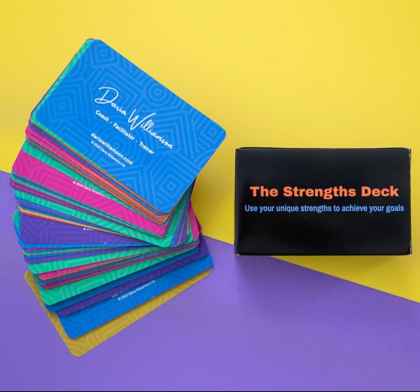 A set of The Strengths Deck cards fanned out so their colourful backs are visible, next to black The Strengths Deck cards box, on a purple and yellow background.