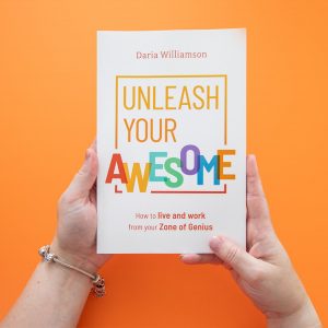 A copy of 'Unleash Your Awesome' by Daria Williamson held by a woman's hands, in front of an orange background.