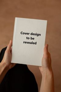 Two hands holding a book with a plain cover and black text 'Cover design to be revealed' superimposed.