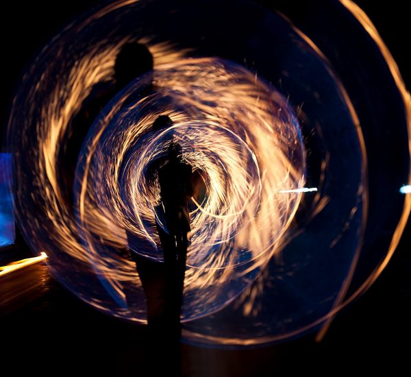 A long-exposure photo of a person twirling a sparkler or similar, creating concentric circles of fire light
