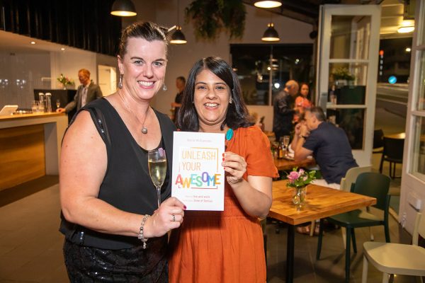Two women smiling at the camera, holding a copy of Unleash Your Awesome